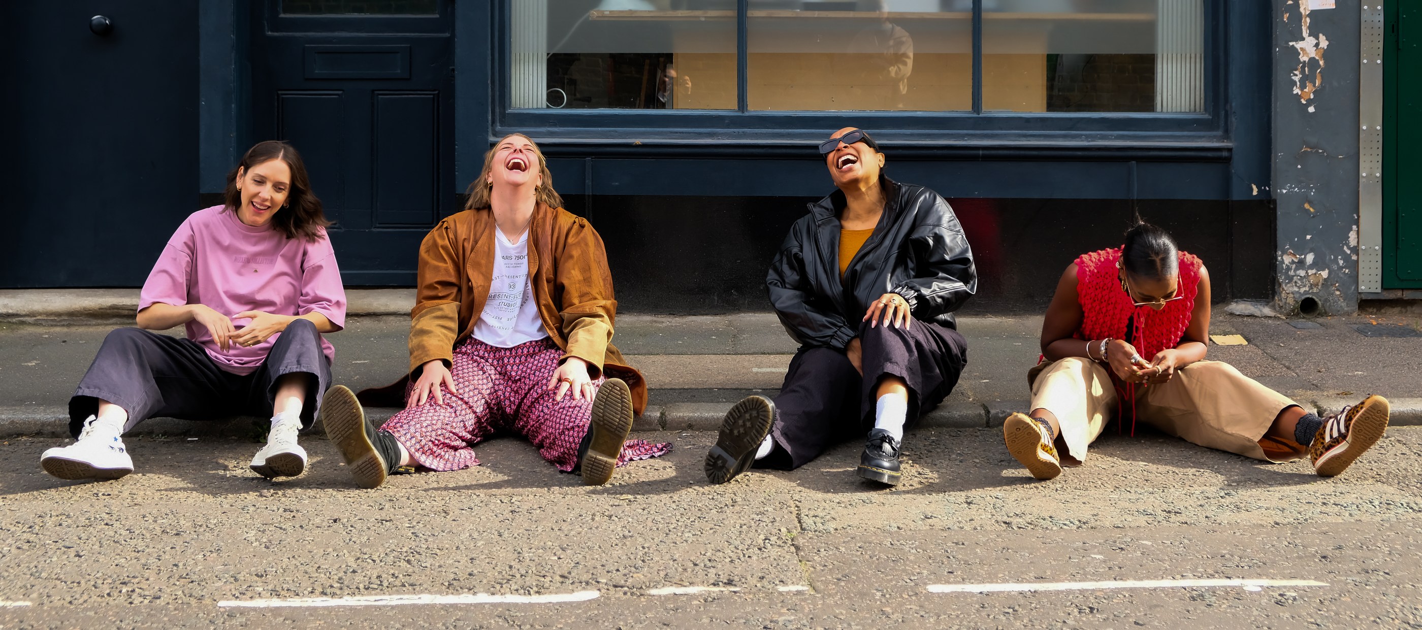 The four hosts of Not Safe For Kids sitting together on a London street